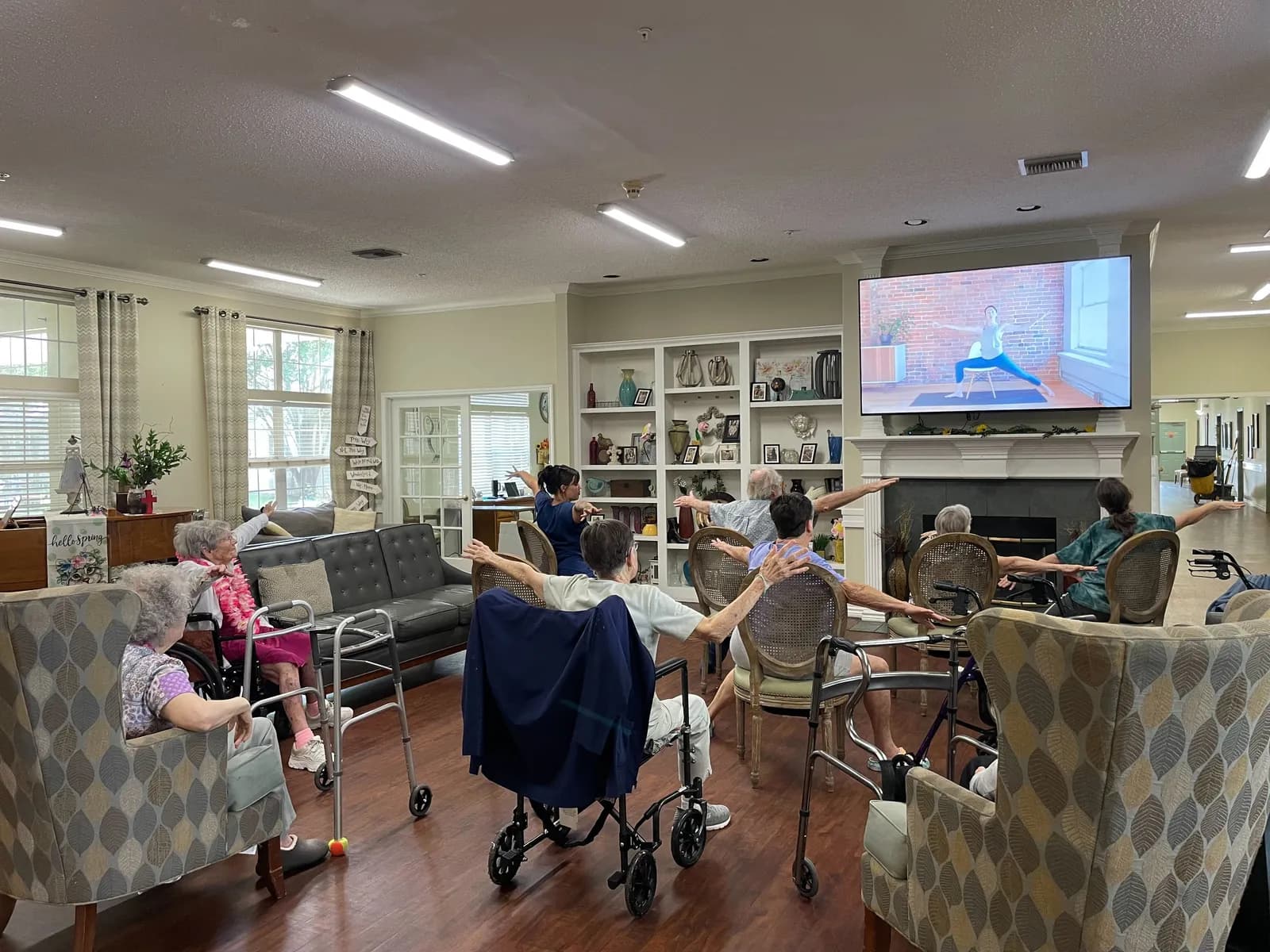 Residents follow along with a seated exercise class in a bright common room at Argent Court