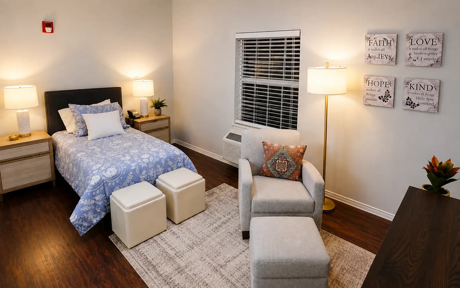 A furnished respite apartment at Argent Court with a made bed, an armchair with ottoman, and warm wall decor